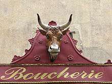 Enseigne traditionnelle de boucherie. Tête de bœuf sur tôle rouge sang