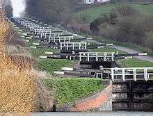 Système d'écluses « en escalier » à Caen Hill (Devizes), sur le canal Kennet-and-Avon, dans le sud de l'Angleterre. Il y a ici 16 écluses séparées par de très courts biefs pour permettre le croisement des bateaux.